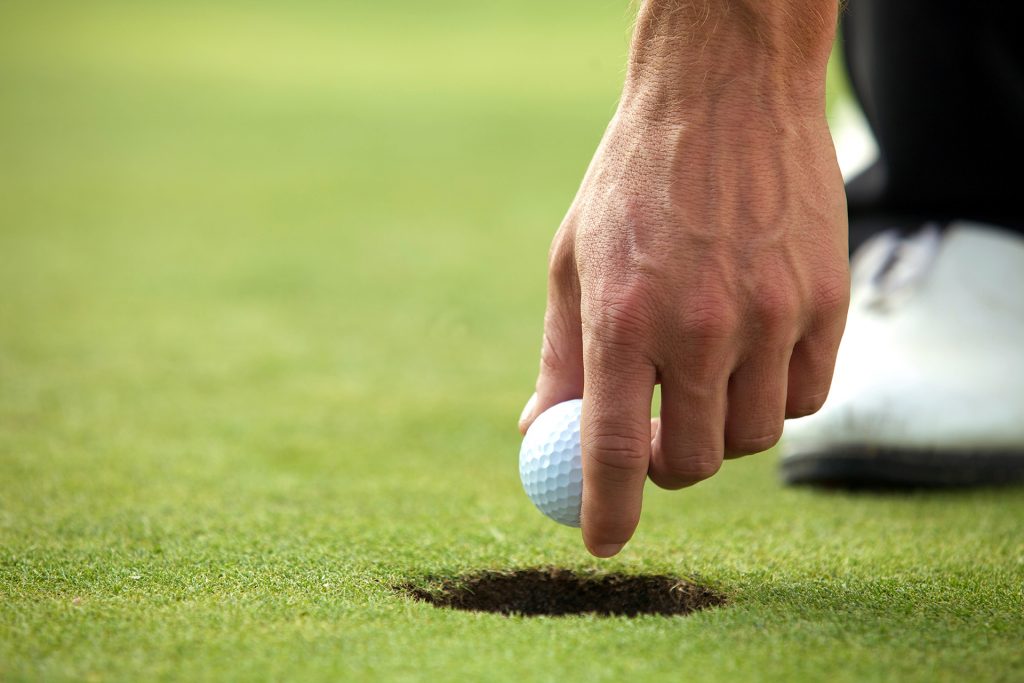 Une main retirant une balle de golf d'un trou