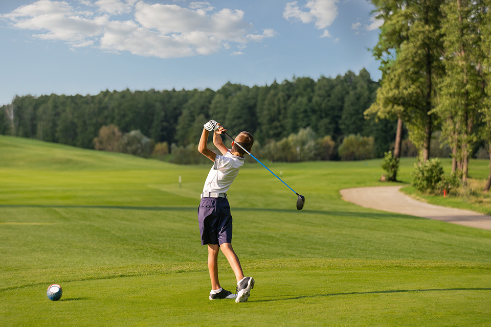 Un garçon de 11 ans frappe une balle de golf sur le té en utilisant un fer