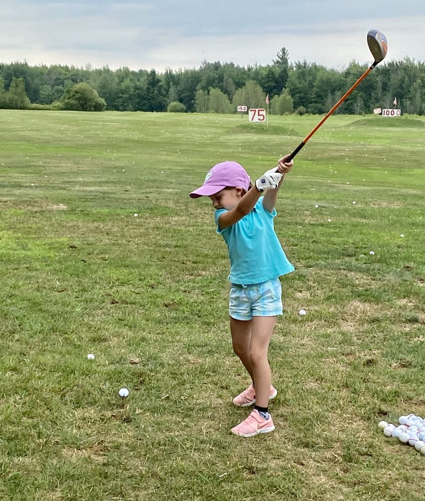 Camp de formation pour enfants : une petite fille se donnant un élan avec un bois pour frapper une balle de golf