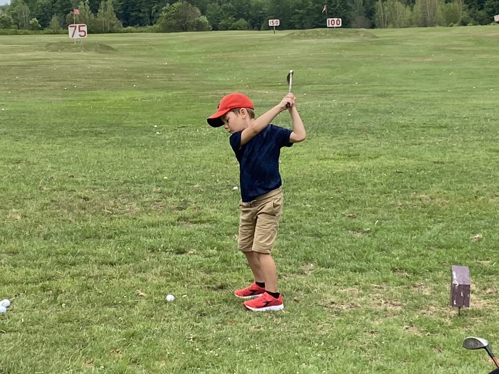 Camp de formation pour enfants : un jeune garçon se donnant un élan avec un fer pour frapper une balle de golf